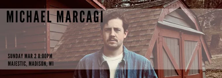 A promotional banner featuring musician Michael Marcagi. The background includes rustic, weathered wooden sheds, while Marcagi, wearing a denim jacket, is positioned in the center. His name appears prominently in bold, uppercase black text on the left. Below his name, event details read: "Sunday Mar 2 8:00PM, Majestic, Madison, WI."